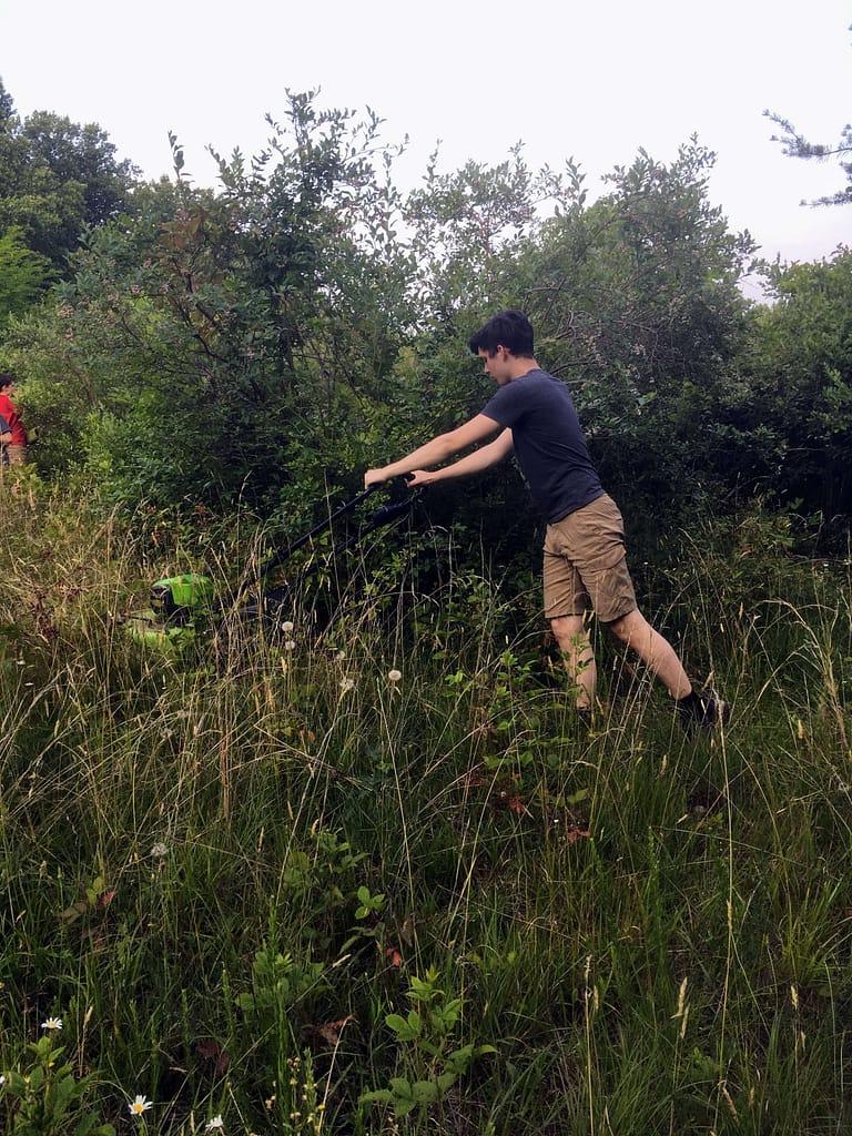 15 year old pushing a lawn mower through a tall field