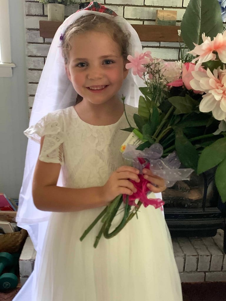 a 6 year old playing wedding with a white dress and big bouquet of flowers