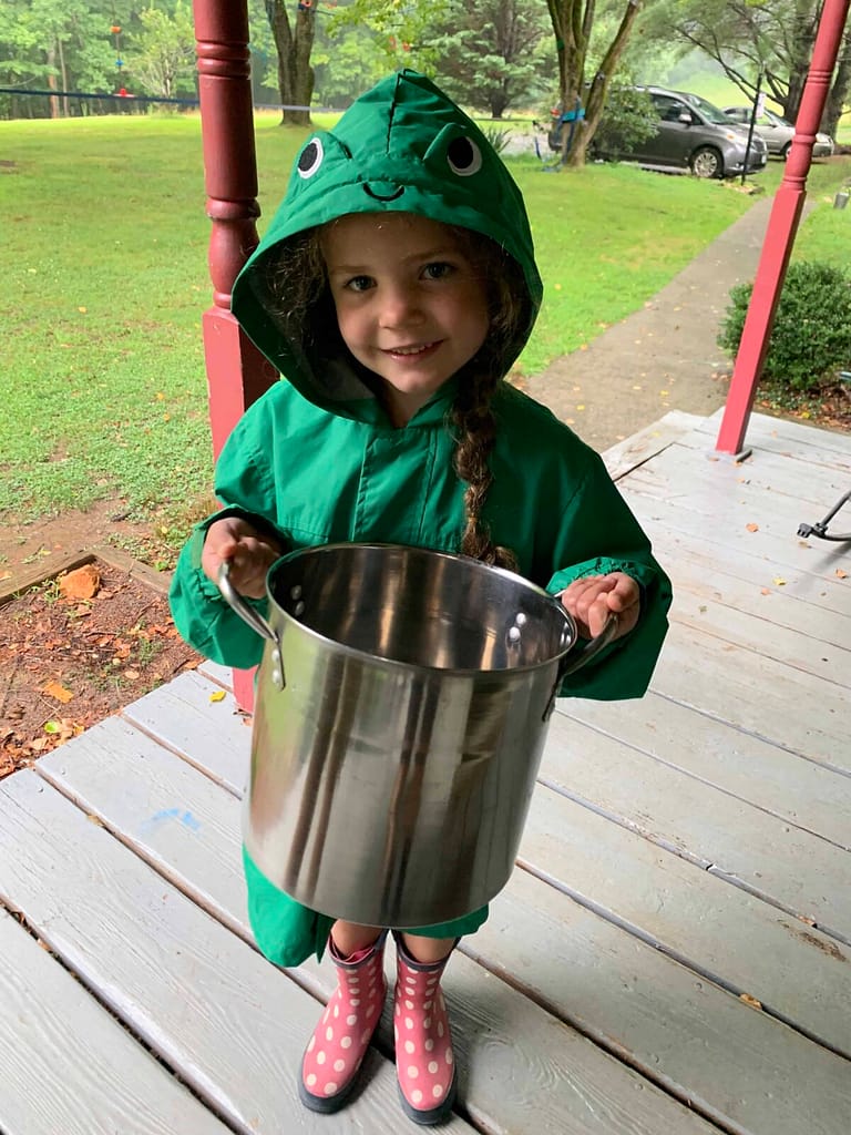 6 year old with a green raincoat on holding a big pot to go milk the cow