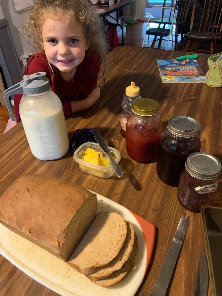 6 year old posing with homemade bread, jam, butter and raw milk