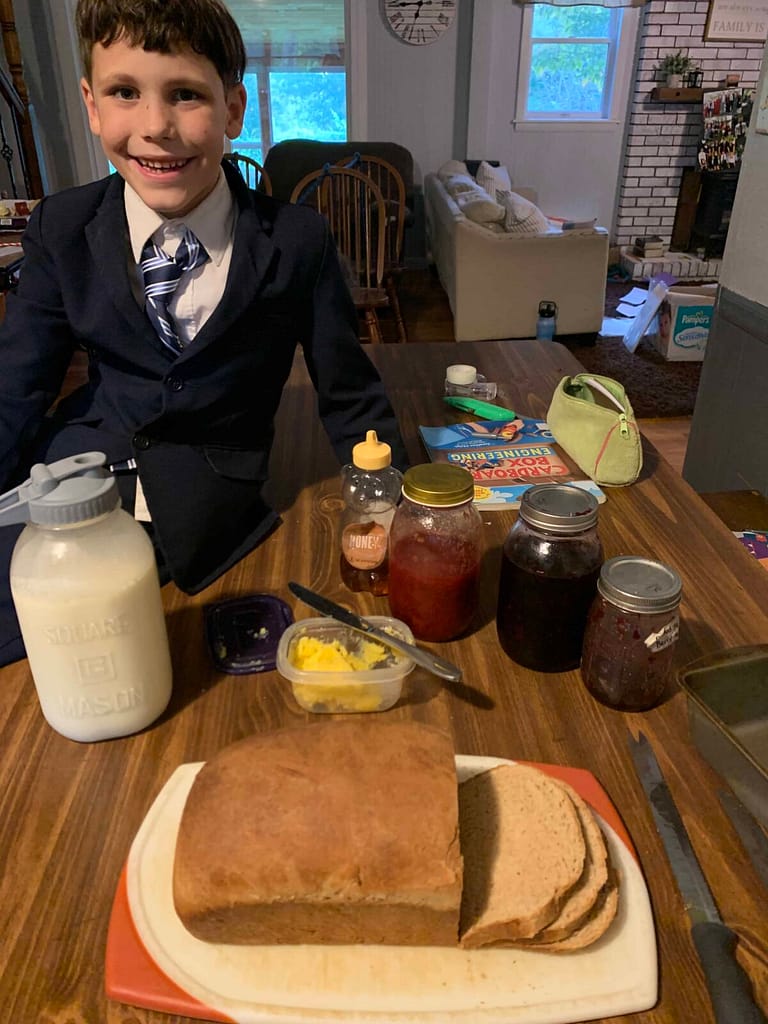 8 year old boy posing next to homemade bread, homemade butter, jam and raw milk
