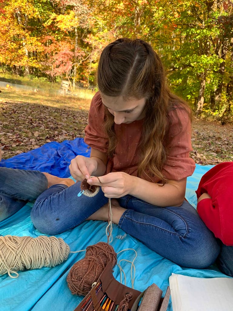 girl crocheting on a blanket in the shade in fall