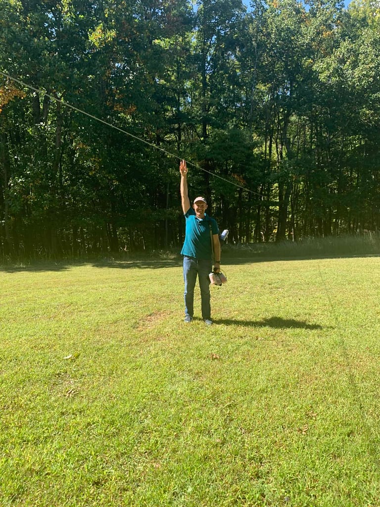 guy standing on grass with his arm up to show how high the zipline is