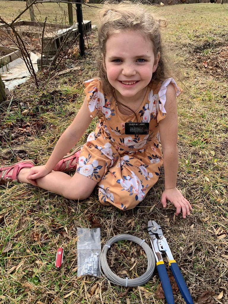 6 year old girl sitting on the grass with tools ready for installing trellis