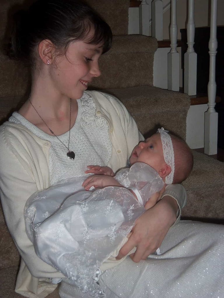 10 year old holding newborn baby sister dressed in white