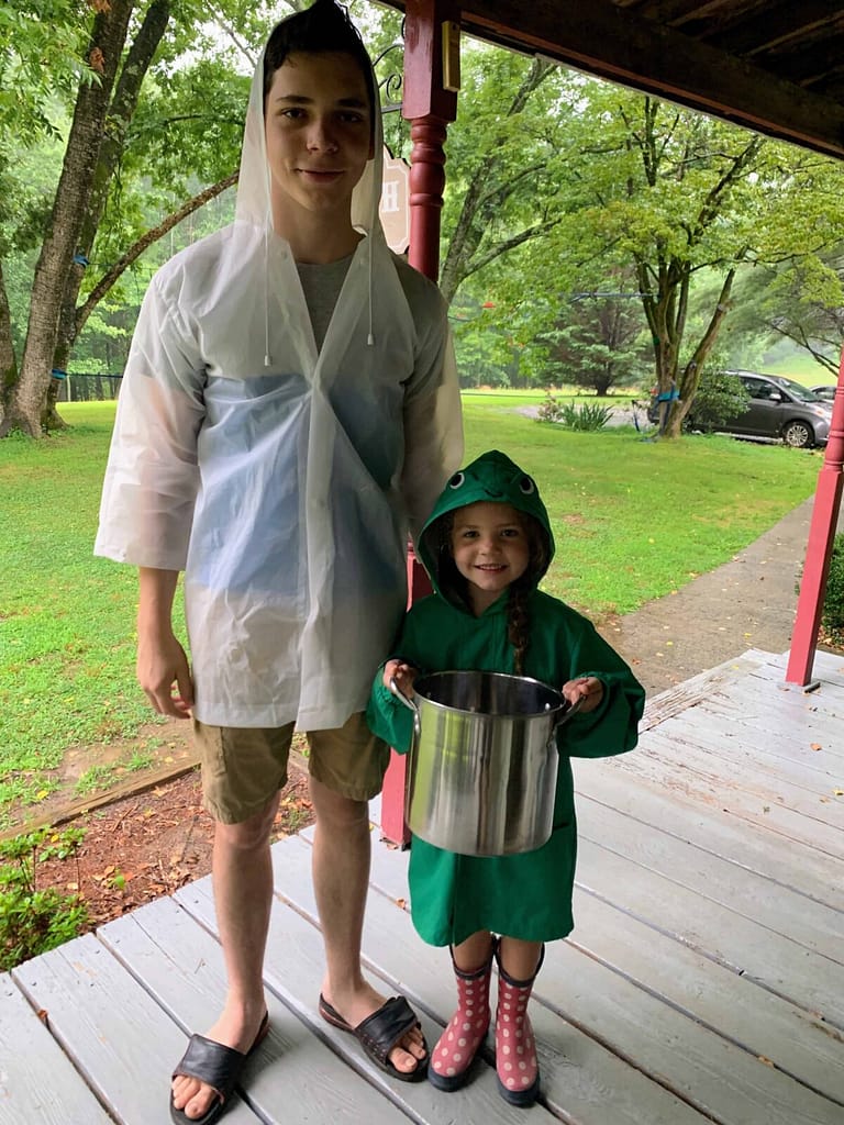 16 year old brother and 6 year old sister wearing rain coats and about to go milk the cow in a summer storm
