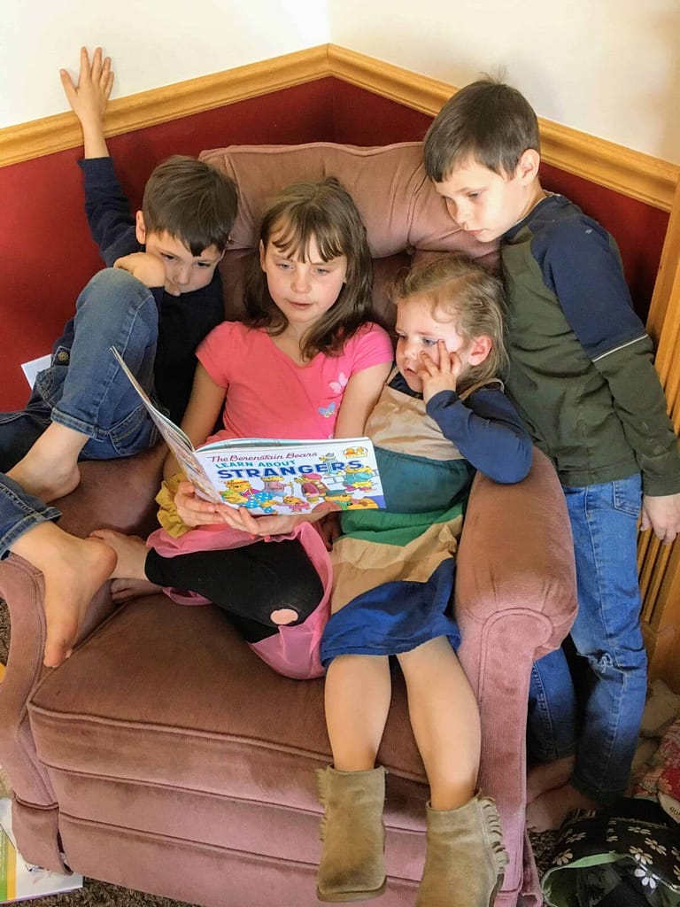 big sister reading to 3 younger siblings on a recliner couch