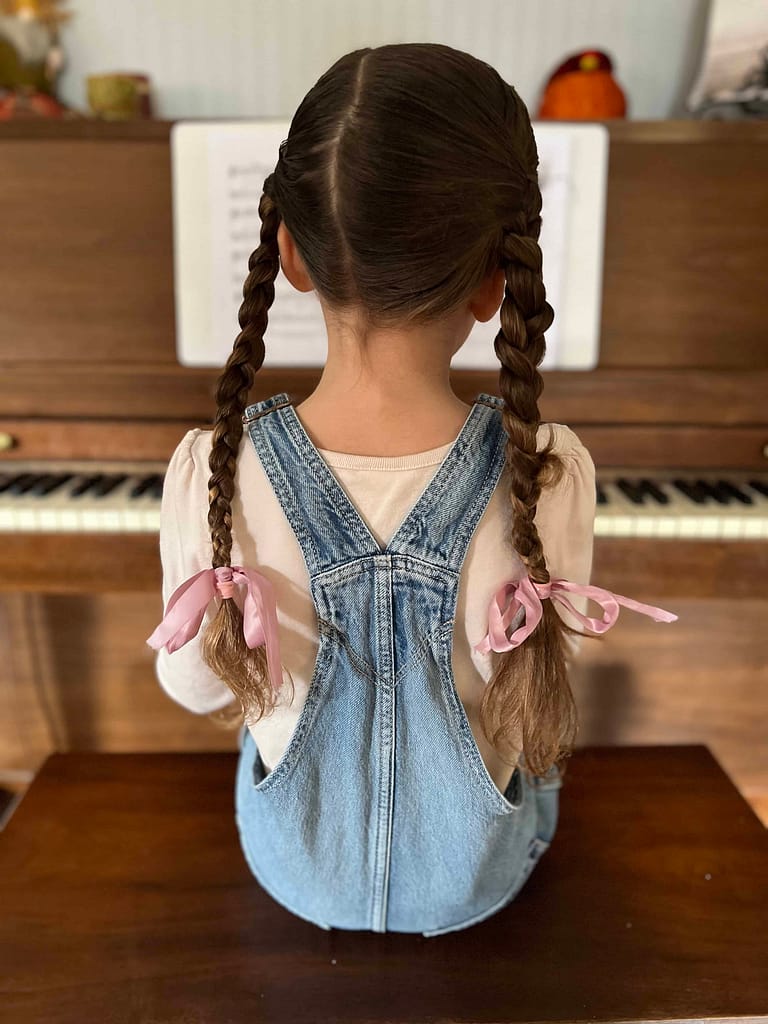 back of girl in overalls and braids playing the piano