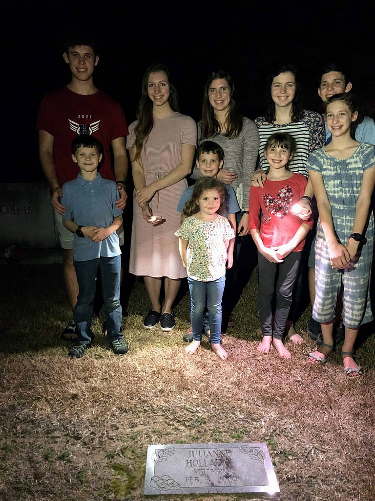 family of 10 children standing by stillborn sister's grave in the dark