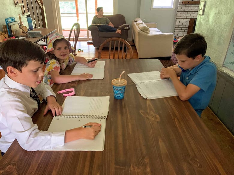 3 kids sit at the kitchen table writing in their journals