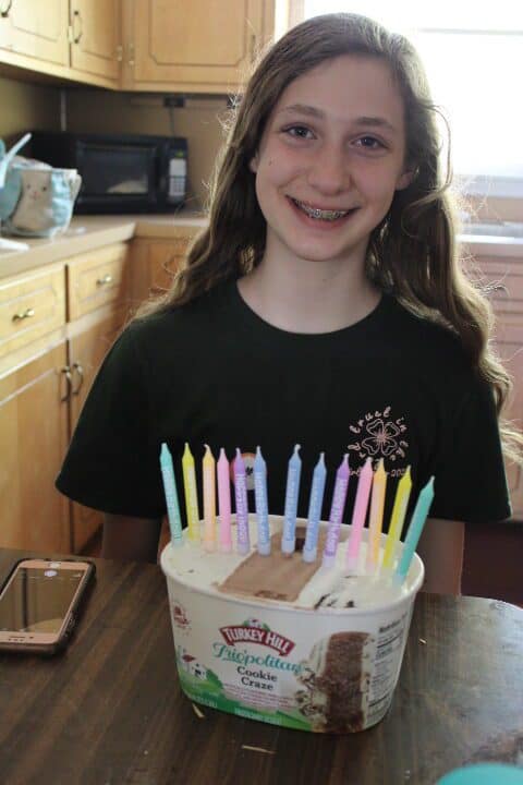 13 year old smiles with 13 candles in her ice cream carton.