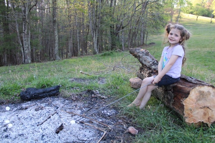 5 year old girl sits on a log and roasts a marshmallow
