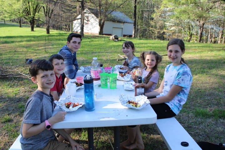 family with 6 kids eating foil dinners at a picnic table in spring.