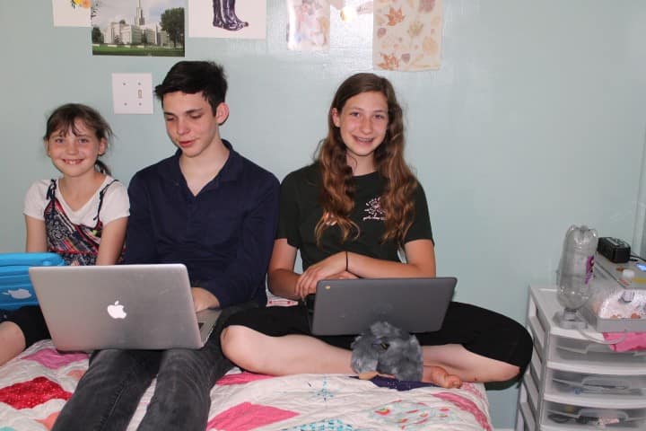 3 kids write music on computers while waiting by an incubator for chicks to hatch.