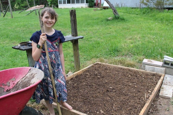 girl standing next to a raised garden bed she just got ready to plant