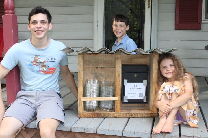 3 kids showing off the blueberry stand they made