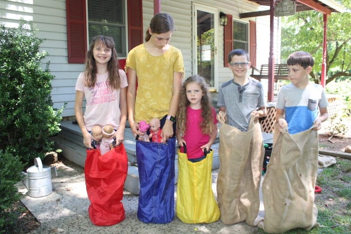 5 siblings do a sack race with their dolls
