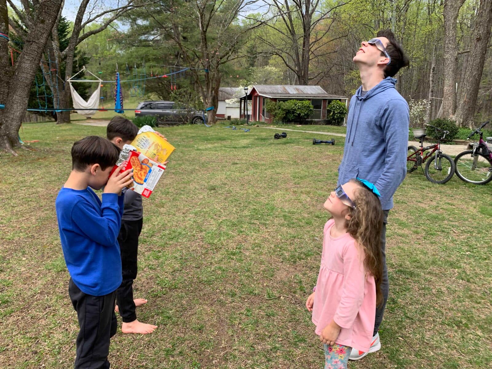 two kids looking through solar eclipse glasses and two looking through solar boxes